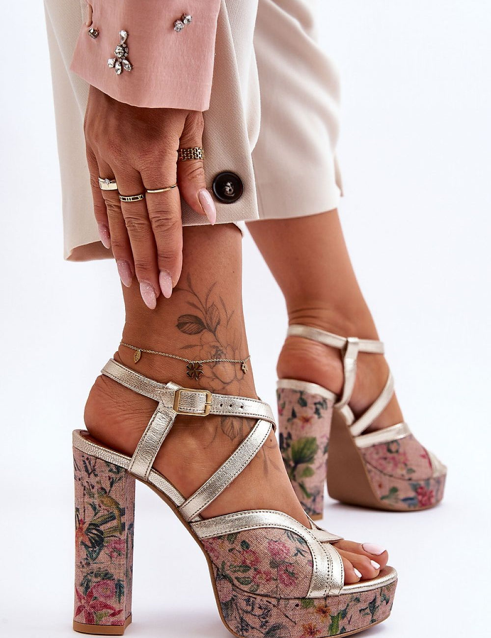 Close-up of floral-patterned, high-heeled sandals paired with elegant pink trousers, showcasing modern fashion footwear.