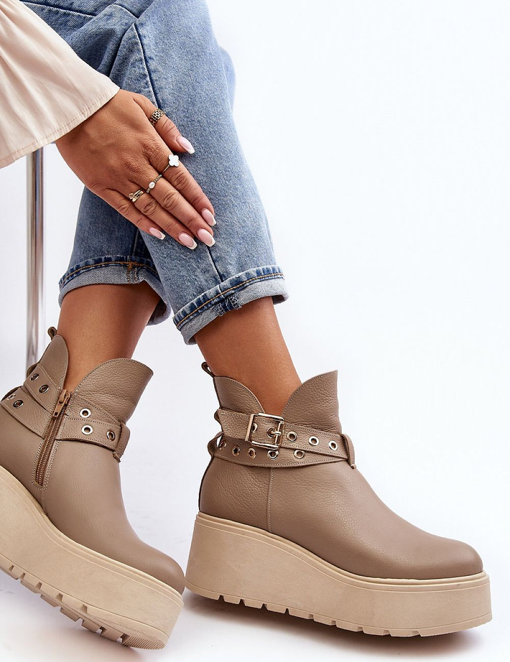 Stylish beige platform ankle boots with metal eyelet straps, paired with rolled-up jeans for a chic, casual look.