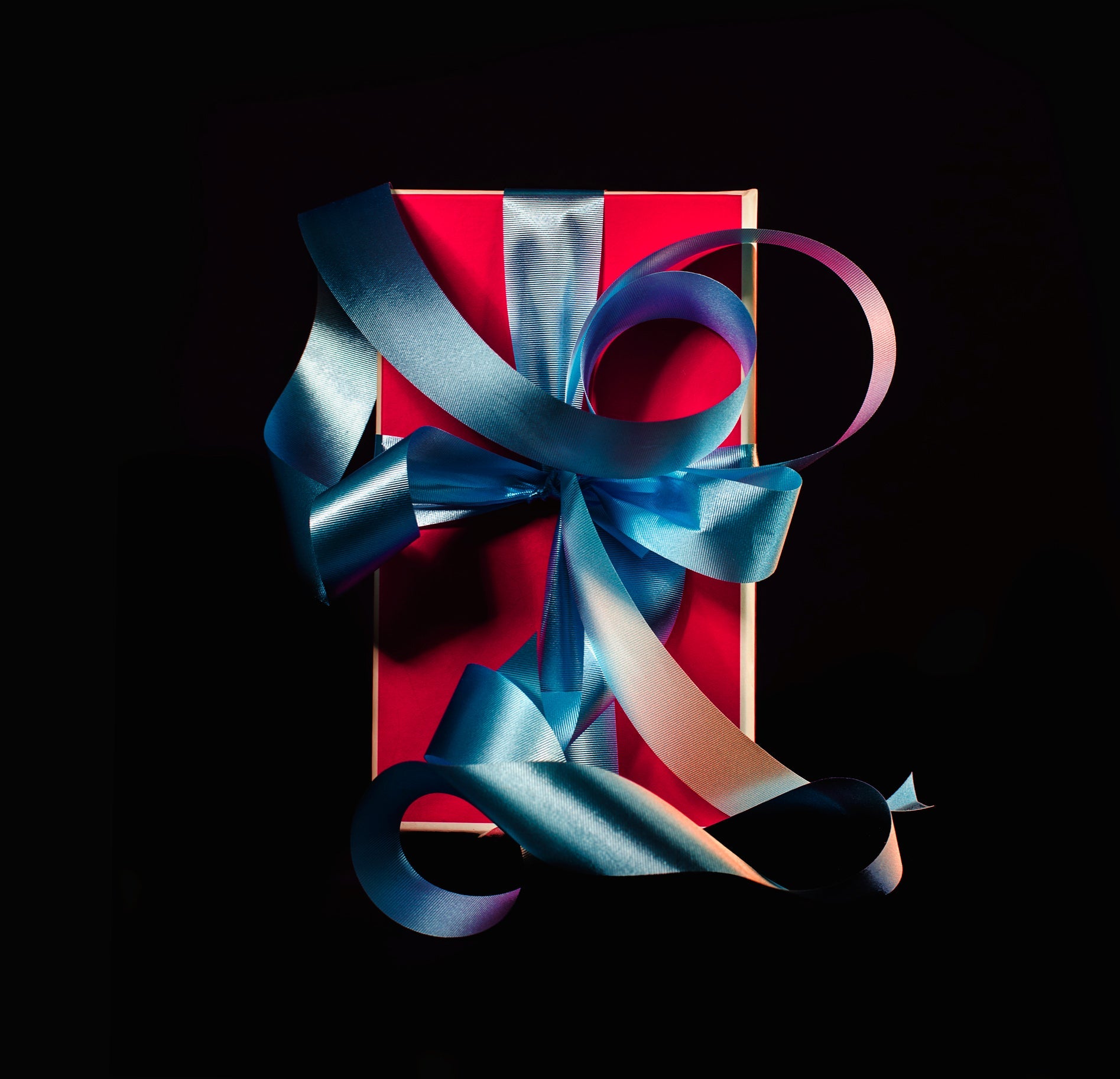 Red gift box with a large blue ribbon on a dark background, perfect for special occasions and celebrations.