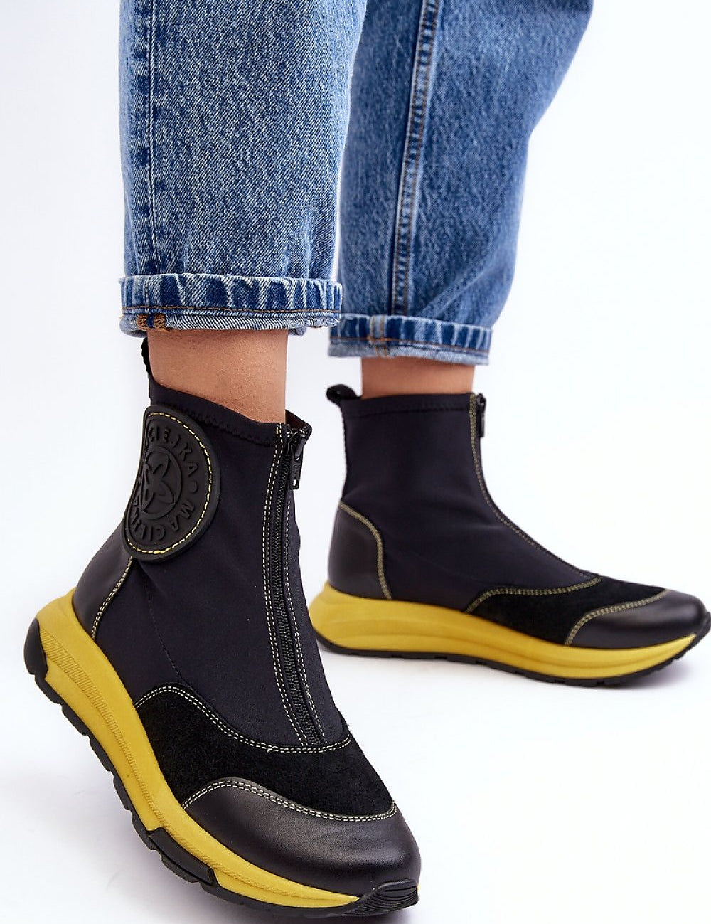Ravena Leather Sport-Zip Boots with bold yellow sole, featuring a modern silhouette and front zipper, styled with blue denim jeans.
