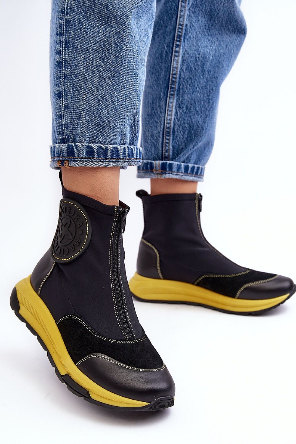 Ravena Leather Sport-Zip Boots with bold yellow sole, featuring a modern silhouette and front zipper, styled with blue denim jeans.