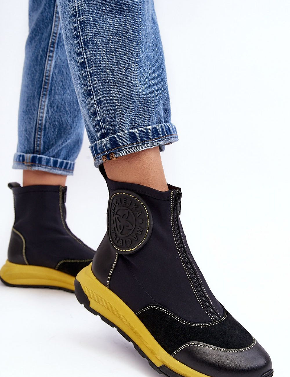 Person wearing Ravena Leather Sport-Zip Boots with black upper and yellow sole, paired with blue jeans, showcasing sporty modern style.