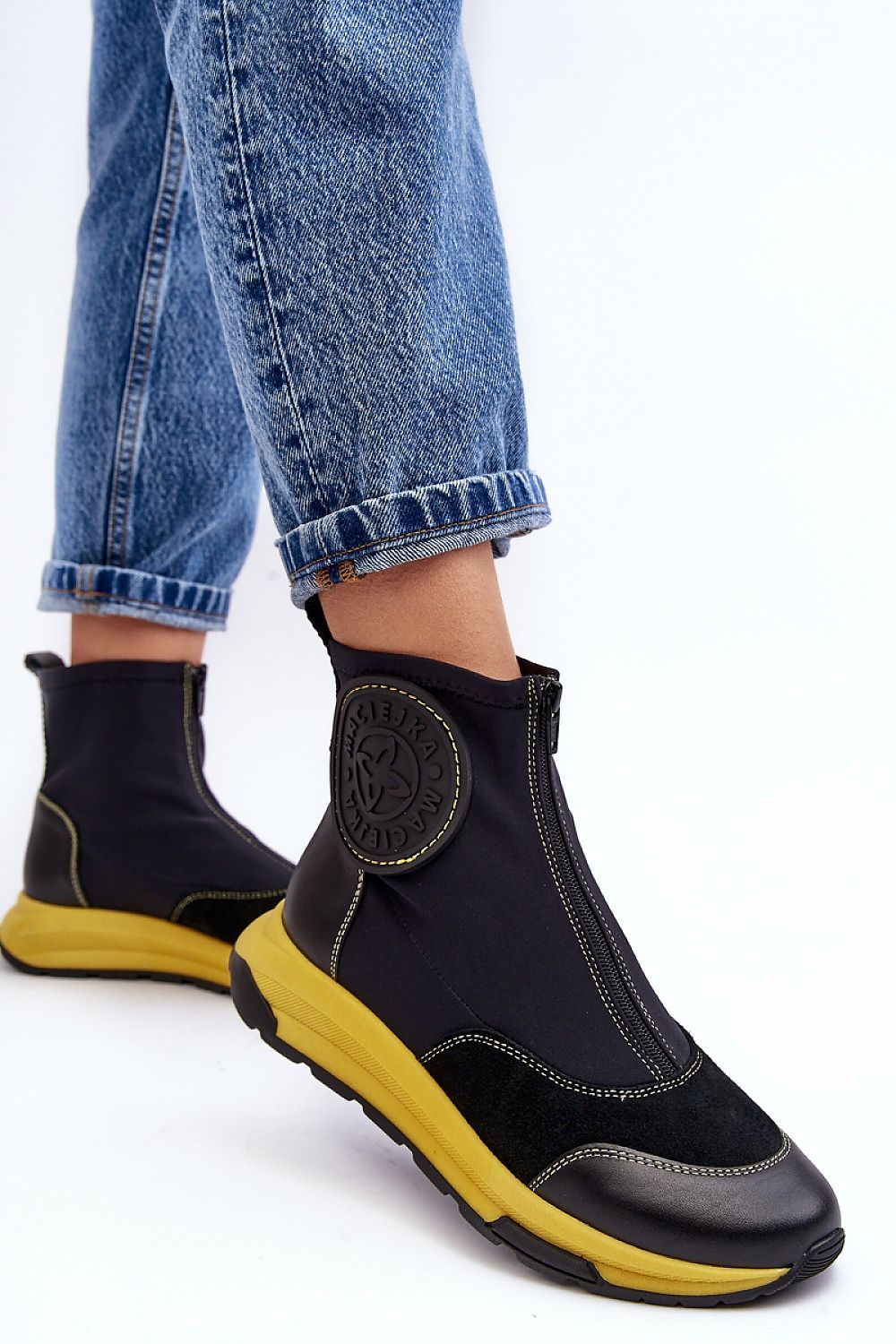 Person wearing Ravena Leather Sport-Zip Boots with black upper and yellow sole, paired with blue jeans, showcasing sporty modern style.