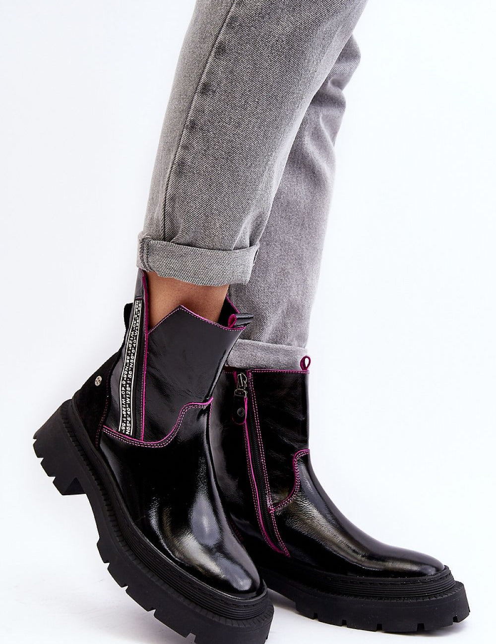 Stylish black leather ankle boots with pink accents and chunky soles paired with rolled-up gray jeans.