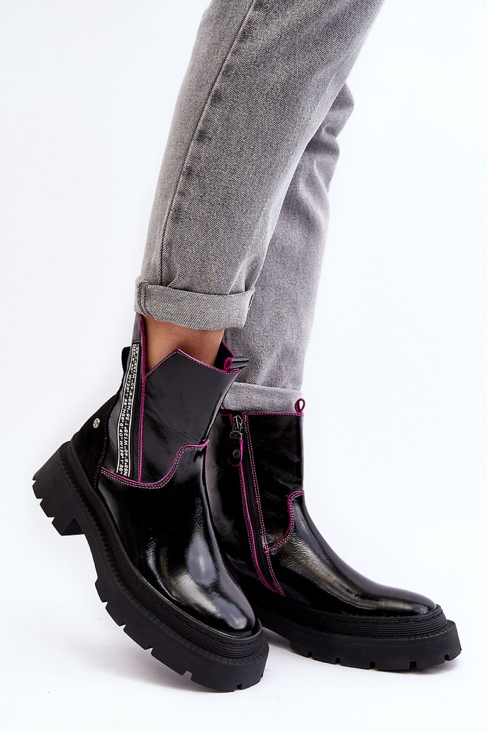 Stylish black leather ankle boots with pink accents and chunky soles paired with rolled-up gray jeans.