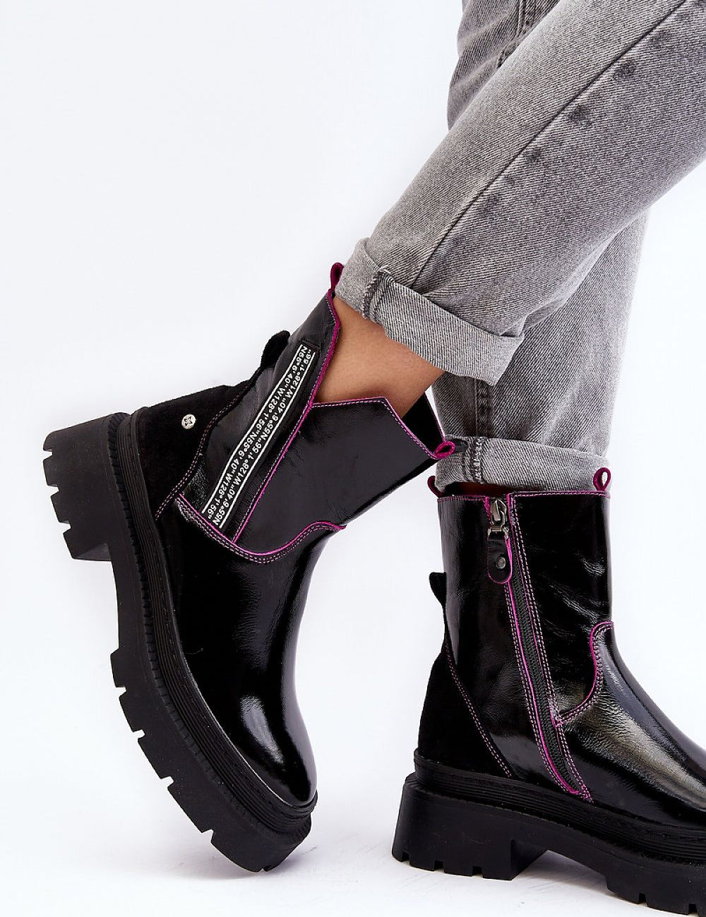 Black leather ankle boots with pink trim, featuring a chunky sole and side zipper. Styled with rolled-up jeans for a casual look.