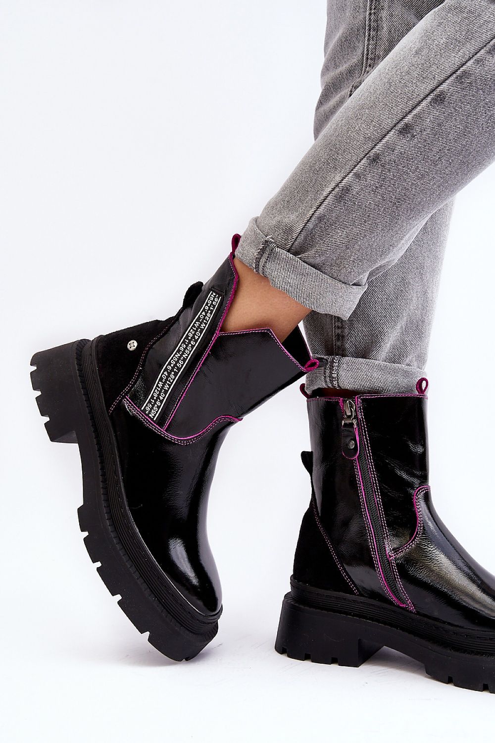 Black leather ankle boots with pink trim, featuring a chunky sole and side zipper. Styled with rolled-up jeans for a casual look.