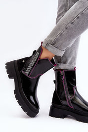 Black leather ankle boots with pink trim, featuring a chunky sole and side zipper. Styled with rolled-up jeans for a casual look.
