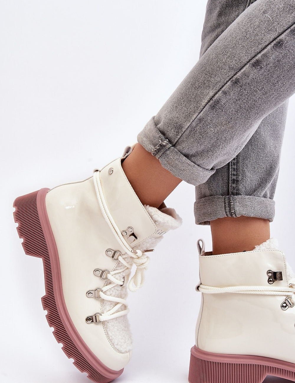 Casual winter boots with lace-up design on an individual wearing rolled-up jeans against white background.