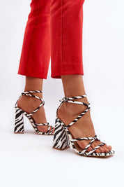 Zebra-print high heel buckled sandals with wide post heel, eco leather upper, and adjustable ankle strap worn with red pants.