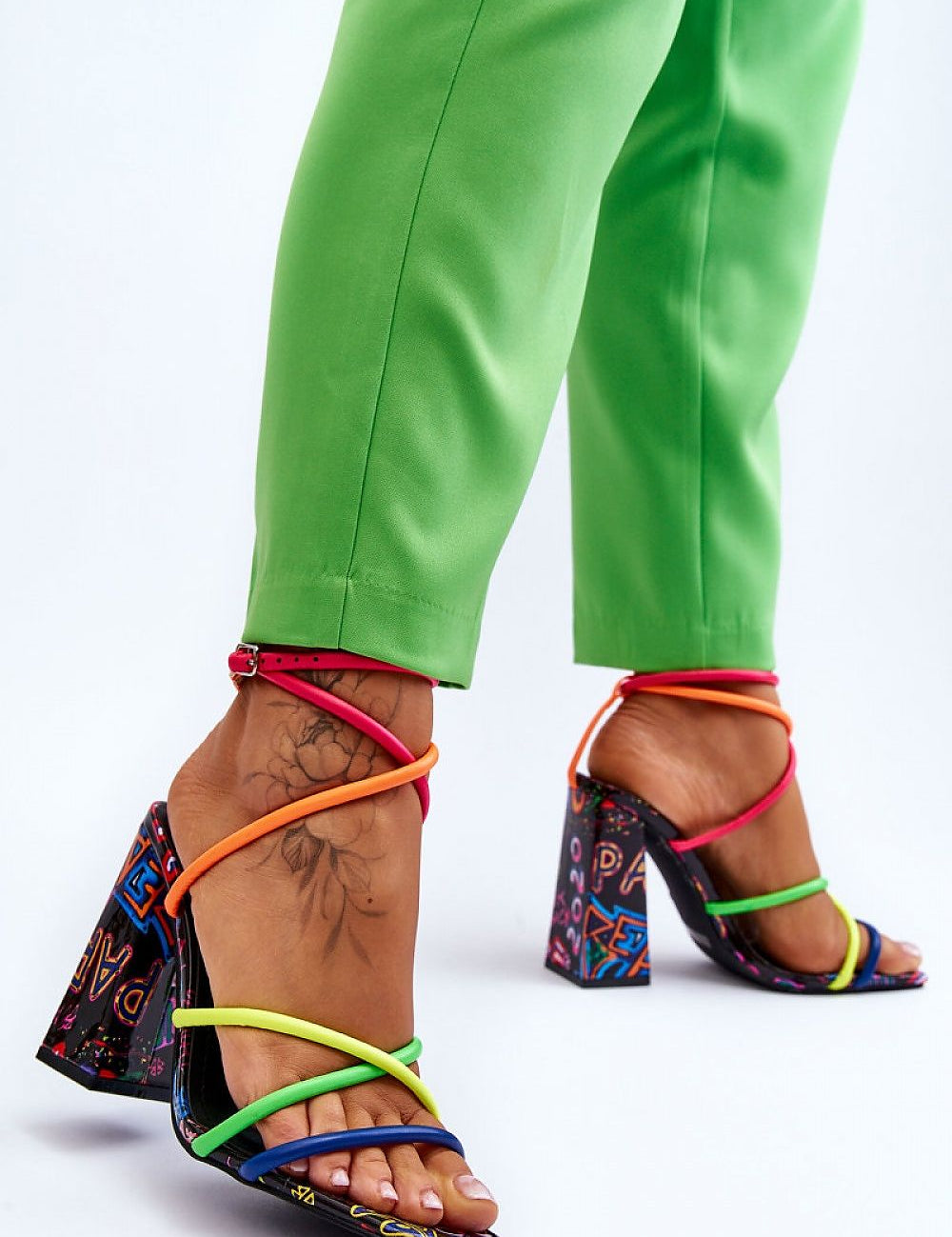 Colorful high heel sandals with strappy design and bold heel, worn with green pants for a vibrant fashion statement.