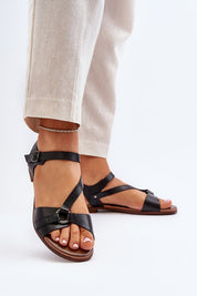 Woman wearing Sylvara classic leather flat sandals in black with adjustable buckle, styled with beige pants for a summer look.