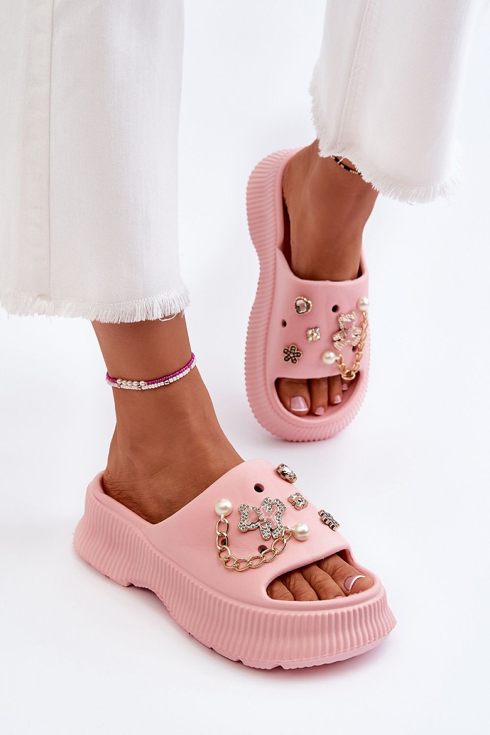 Orminya pink foam platform slides with decorative accents, offering comfort and height, worn with white pants.