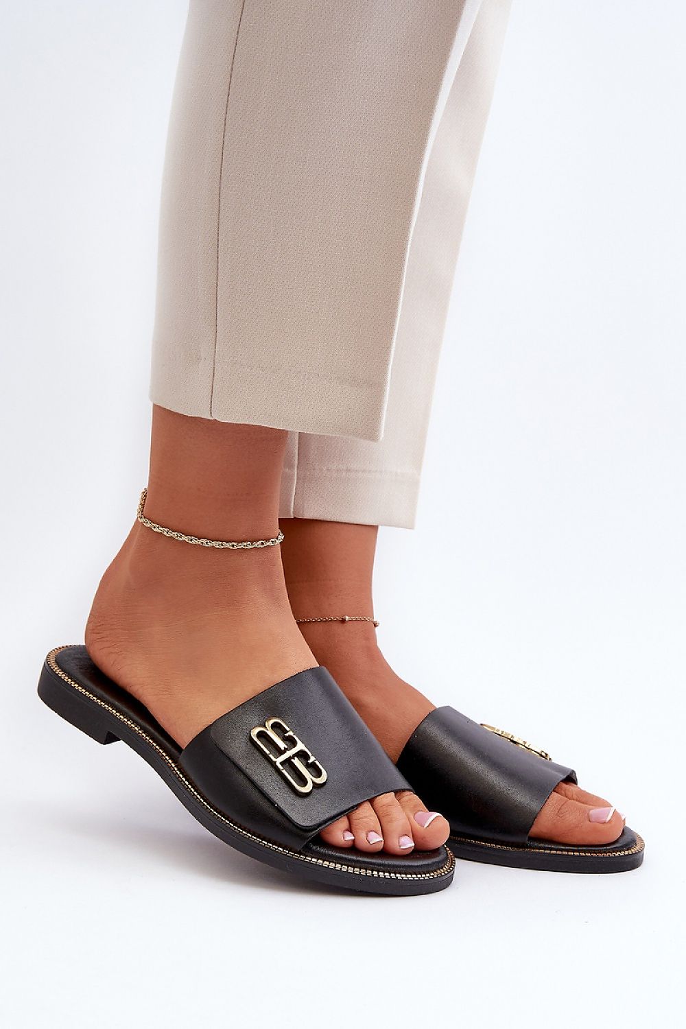 Woman wearing Tavirelle Gold Trim Leather Slides, showcasing sleek design with gleaming gold accent, perfect for warm-season outfits.