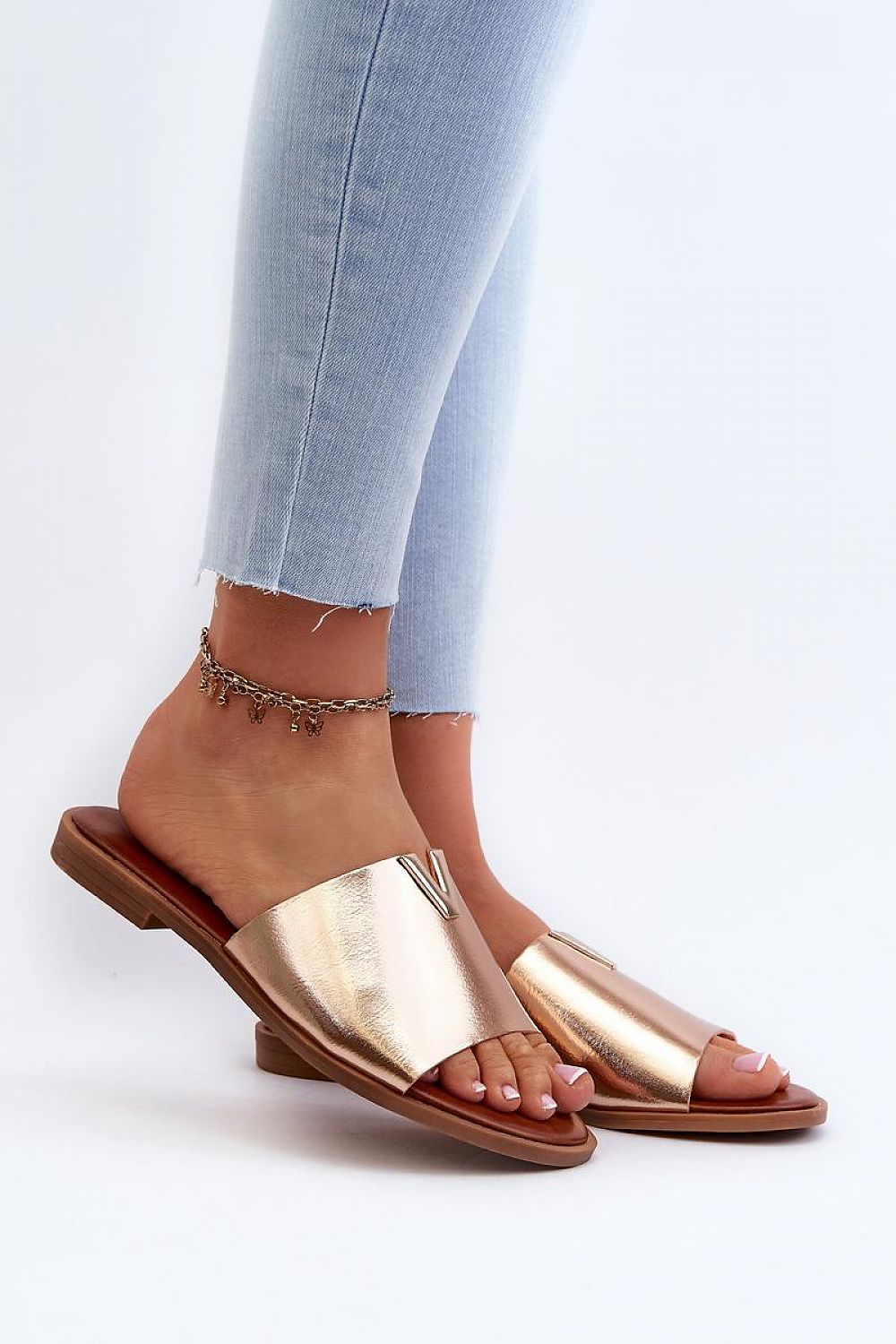 Talvera flat slides in gold on person wearing jeans, featuring eco leather and slim heel, perfect for summer fashion.