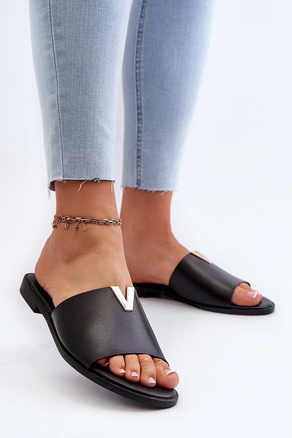 Woman wearing black Talvera flat slides with gold detail, featuring eco leather and a minimalist design, paired with cropped jeans.