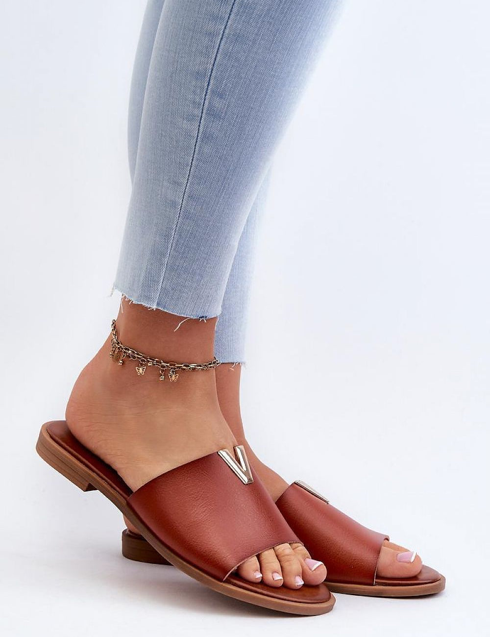 Woman wearing Talvera Flat Slides with gold detail, brown eco leather, paired with light jeans. Minimalist summer sandal style.
