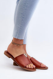 Woman wearing Talvera Flat Slides with gold detail, brown eco leather, paired with light jeans. Minimalist summer sandal style.