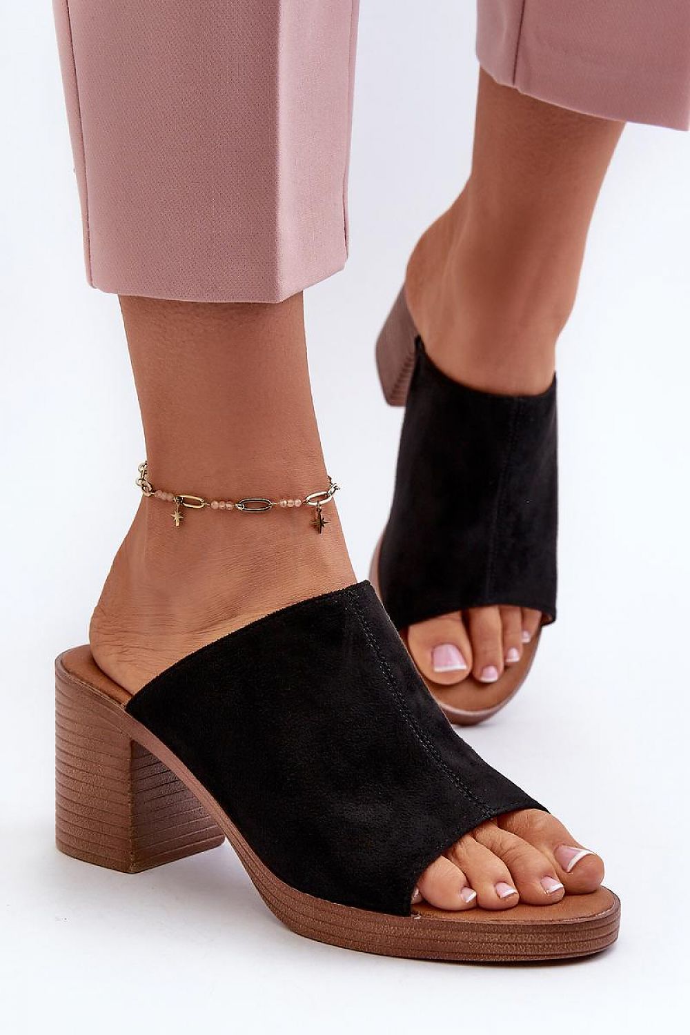 Woman wearing black suede wedge slides with a wooden heel and pink pants, showcasing a stylish anklet.