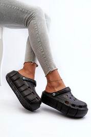 Person wearing black platform foam slides with thick sole, paired with jeans, showcasing the cushioned footwear's sculpted design.