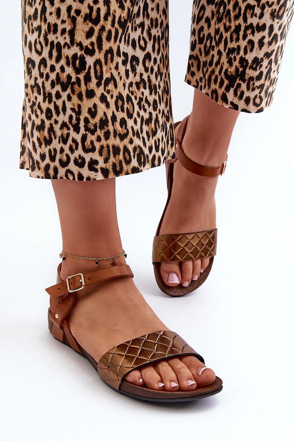 Sorellia Buckled Leather Sandals on model with leopard print pants, featuring adjustable ankle strap and flat quilted design.