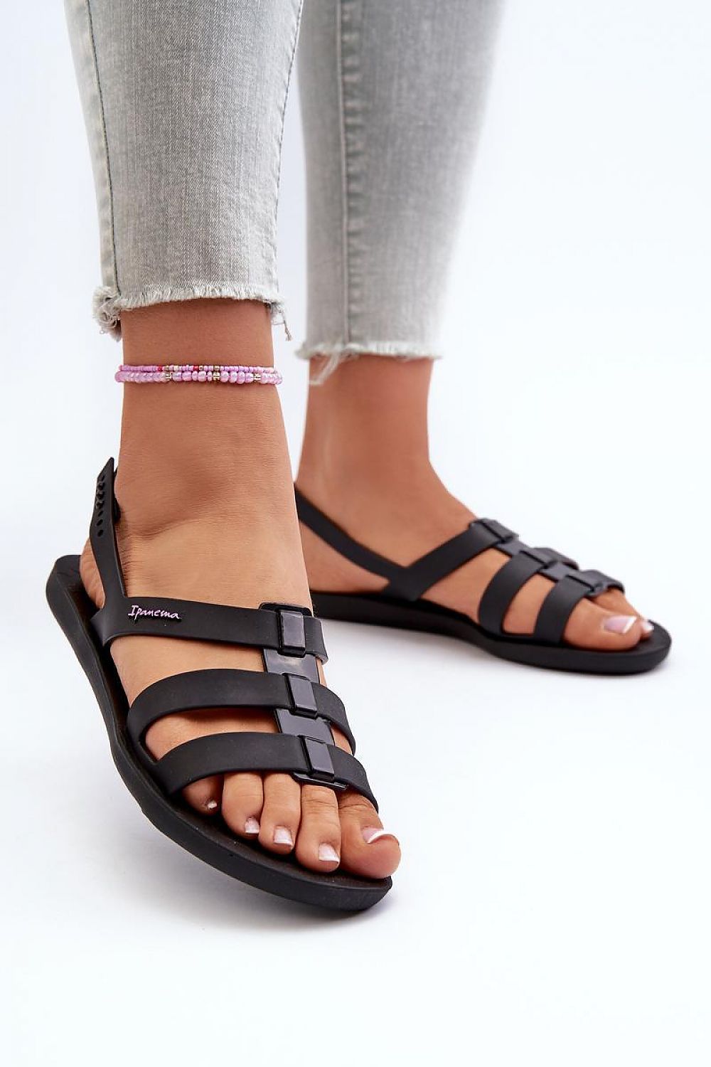 Person wearing Arvia Buckled Poolside Sandals in black rubber with adjustable straps, paired with light jeans and ankle bracelet, perfect for summer.