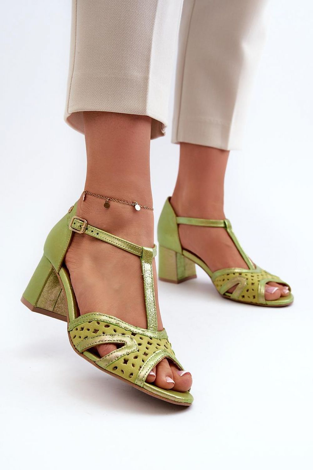 Green leather sandals with block heel and ankle strap, worn with beige pants, showcasing a stylish and comfortable design.