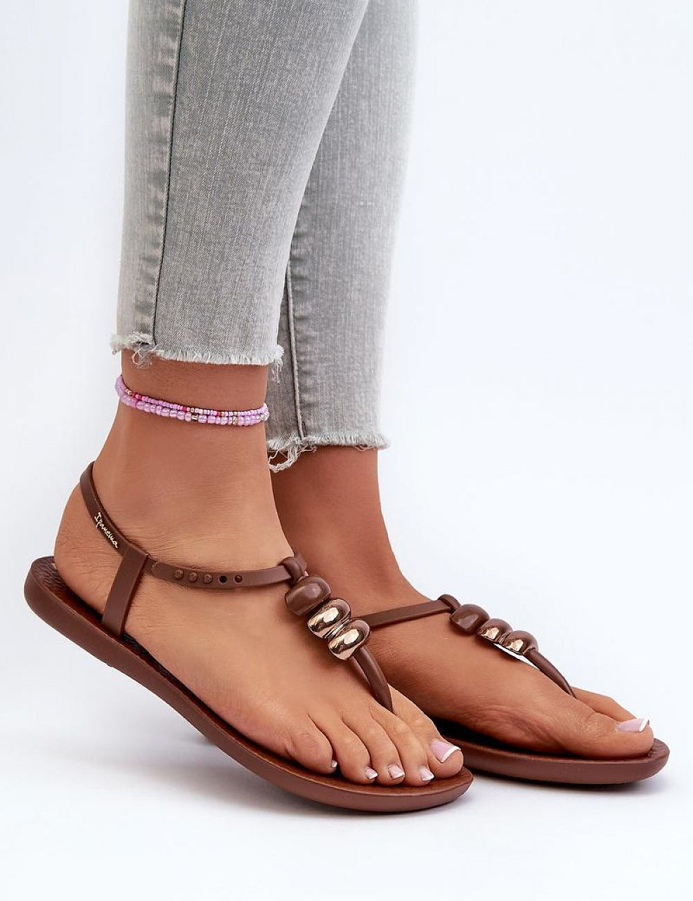 Close-up of Sorela Buckle-Strap Rubber Sandals in brown, styled with light jeans, showcasing dual-buckle design and flat sole.