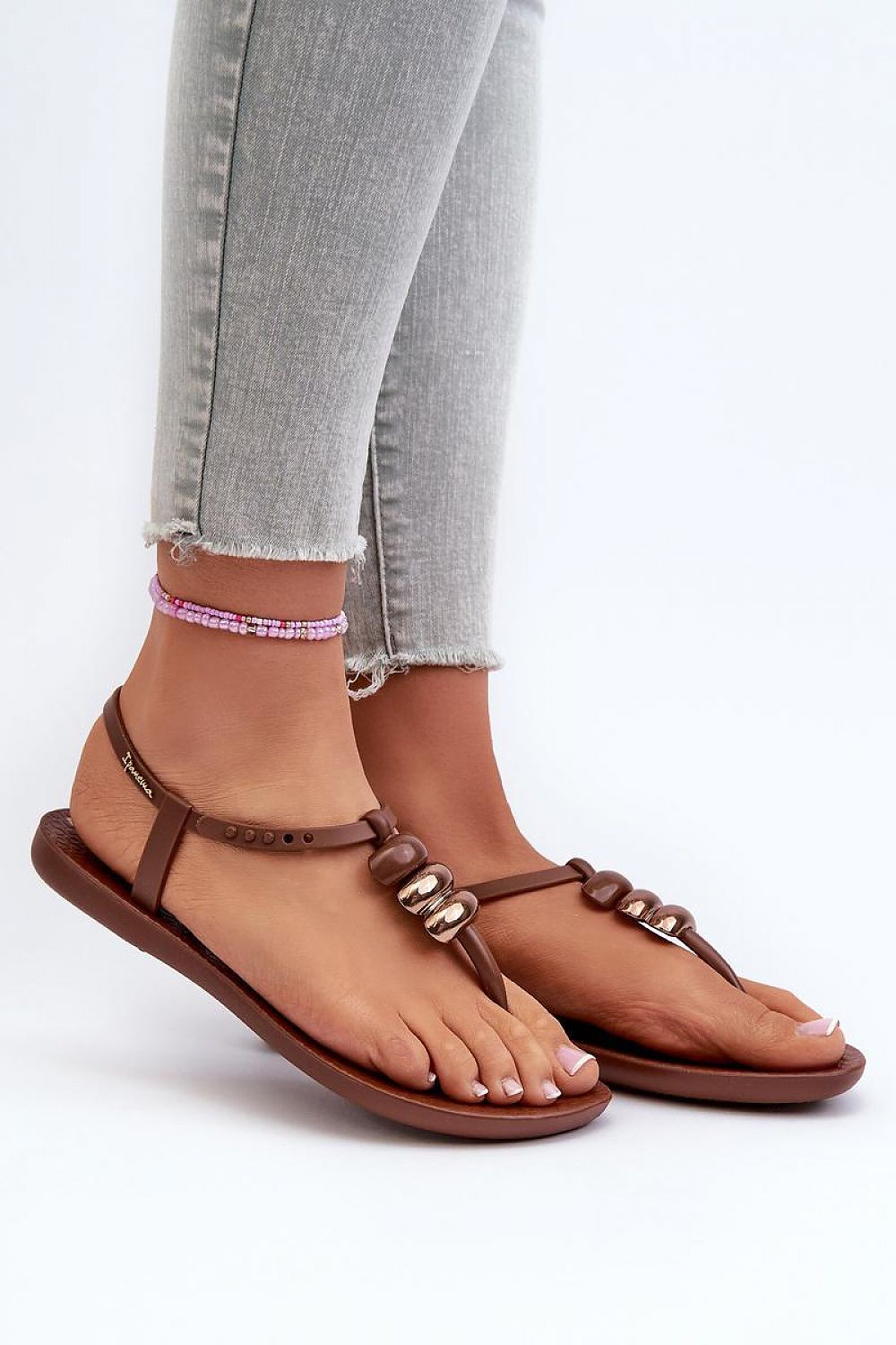 Close-up of Sorela Buckle-Strap Rubber Sandals in brown, styled with light jeans, showcasing dual-buckle design and flat sole.