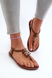 Brown buckle-strap rubber sandals on feet, paired with frayed hem jeans, showcasing a sleek and modern summer look for women.