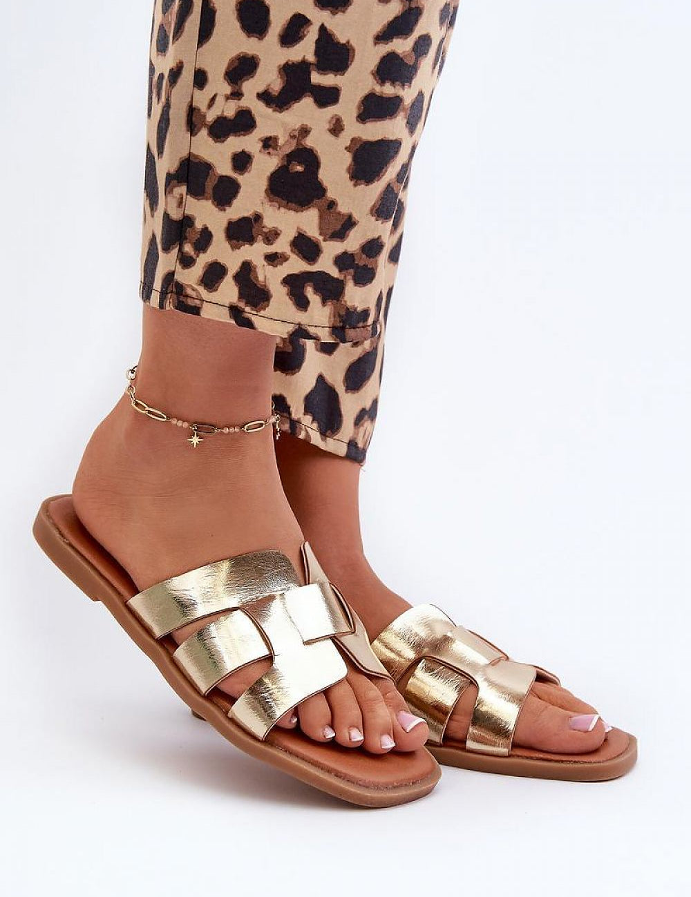Gold metallic sandals with crisscross straps worn with leopard print pants, showcasing stylish and trendy footwear.