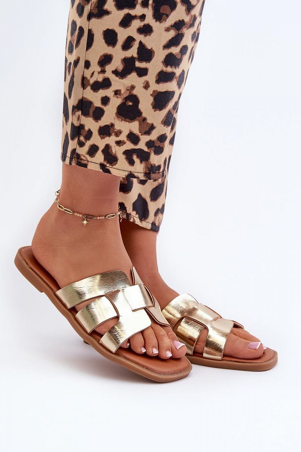 Gold metallic sandals with crisscross straps worn with leopard print pants, showcasing stylish and trendy footwear.