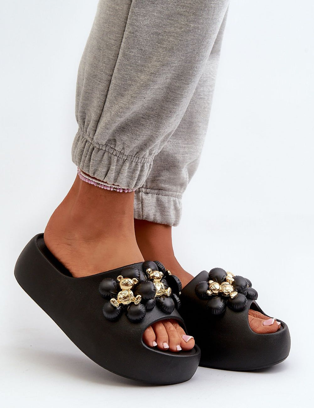 Black platform flip-flops adorned with decorative embellishments, worn with grey joggers; stylish and comfortable footwear.