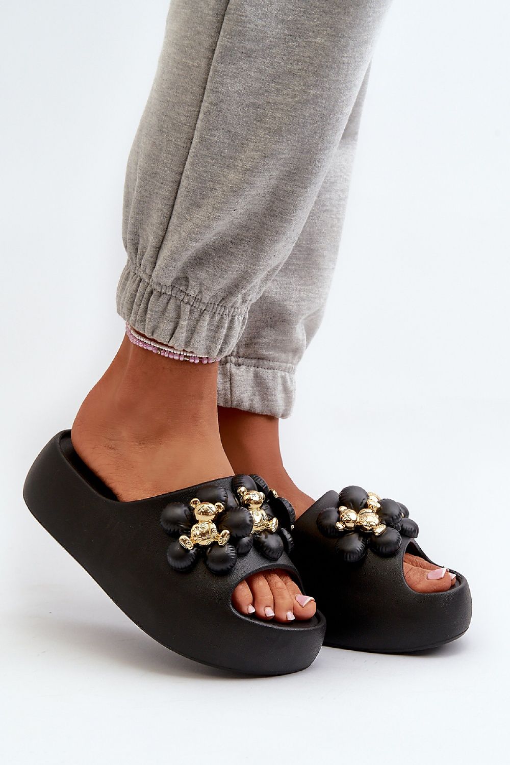 Black platform flip-flops adorned with decorative embellishments, worn with grey joggers; stylish and comfortable footwear.
