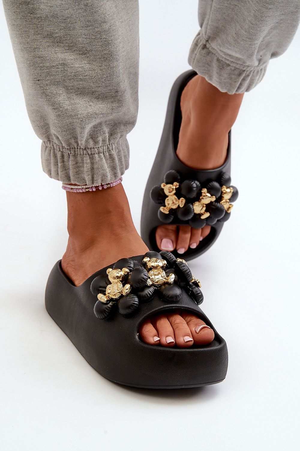 Close-up of black platform flip-flops with gold embellishments, worn with gray pants. Stylish, comfortable summer footwear.