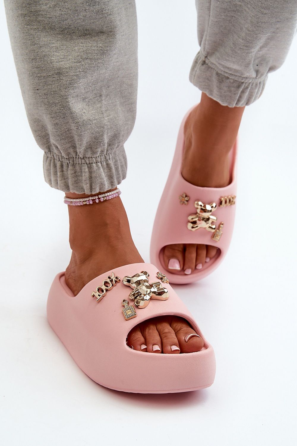 Woman wearing pink foam platform flip-flops with decorative accents, ideal for summer comfort and style, paired with casual sweatpants.