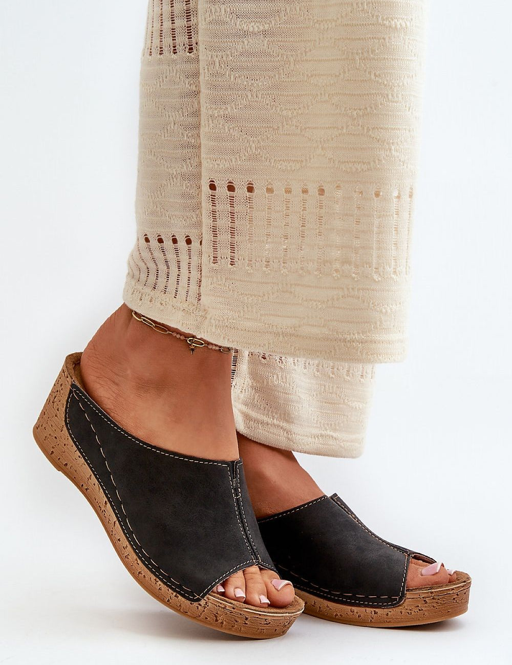 Woman wearing black wedge sandals with beige wide-leg pants on white background