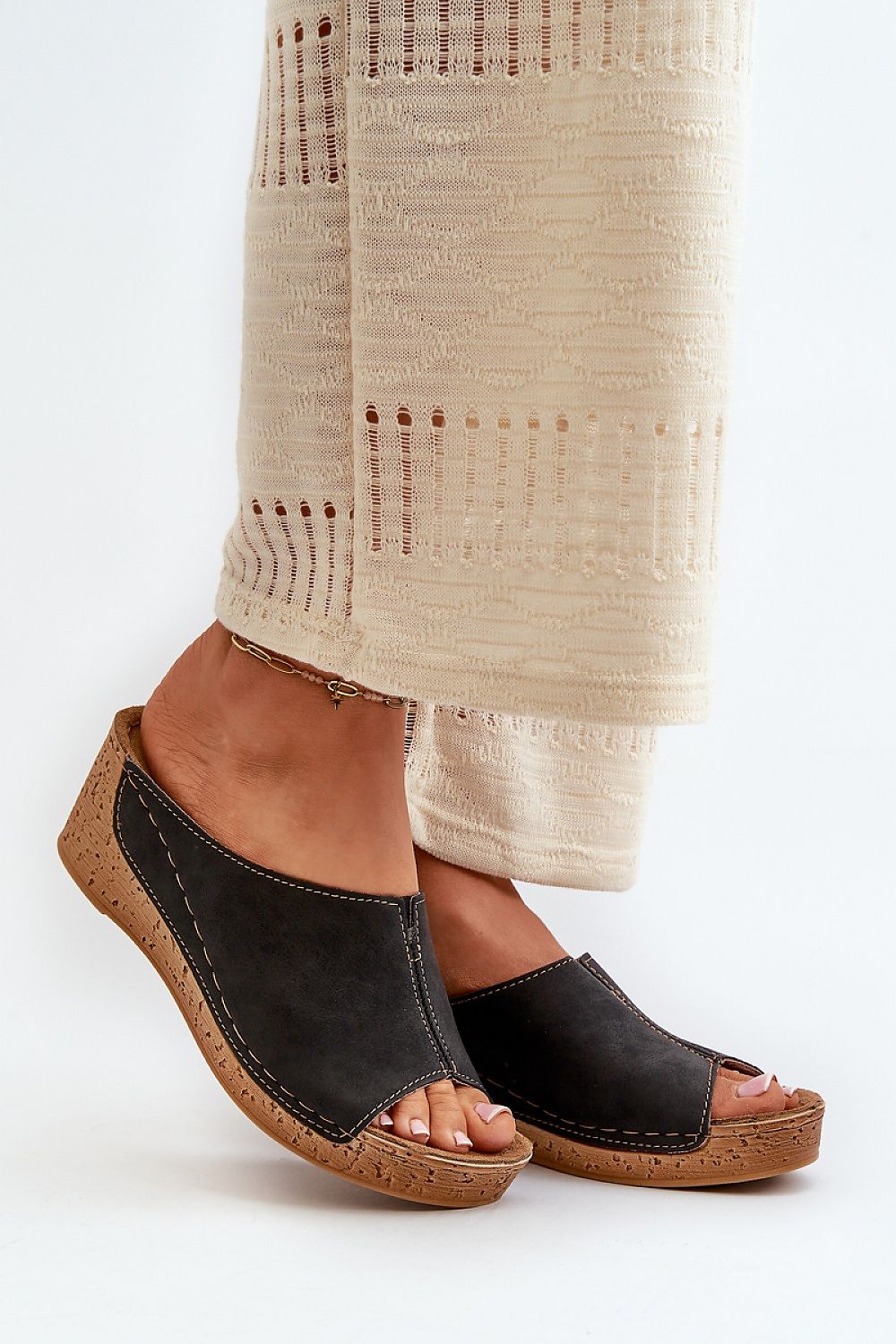 Woman wearing black wedge sandals with beige wide-leg pants on white background