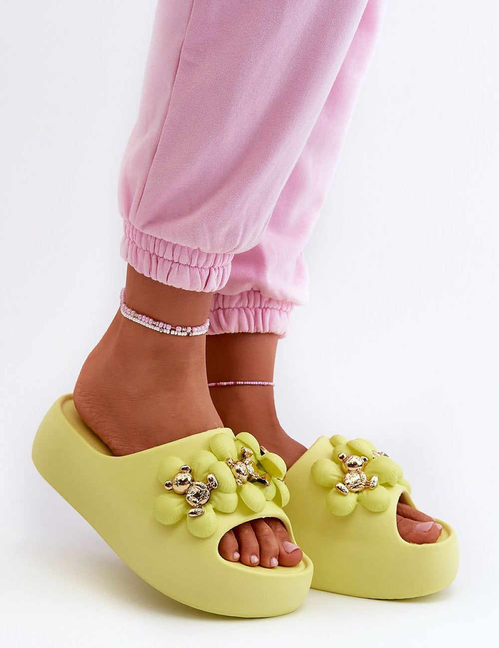 Person wearing green platform flip-flops with decorative accents and pink pants, highlighting comfort and playful style.