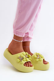 Person wearing green platform flip-flops with decorative accents and pink pants, highlighting comfort and playful style.