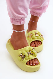 Woman wearing yellow platform flip-flops with decorative embellishments and pink pants, showcasing playful summer footwear style.