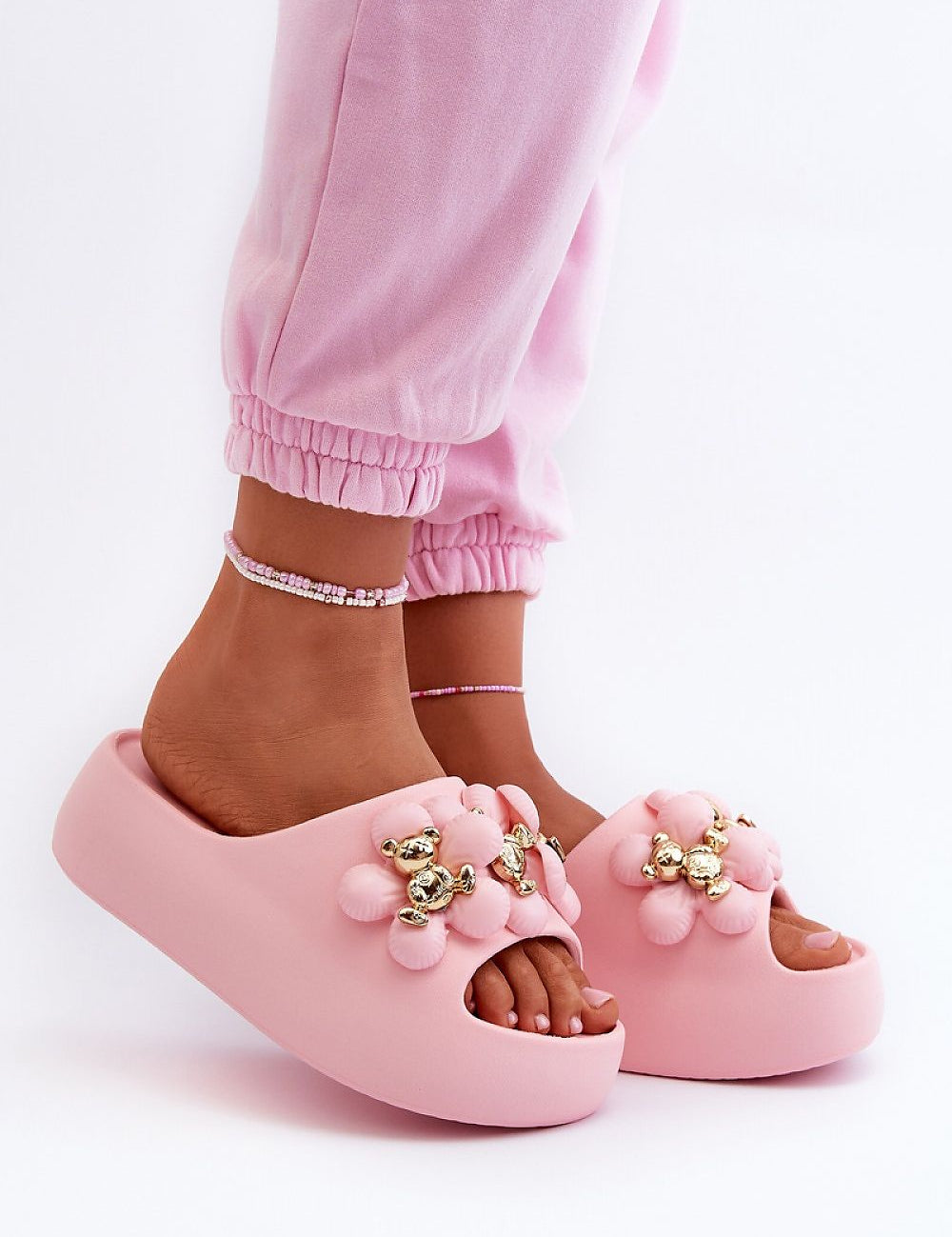 Pink platform summer flip-flops with decorative accents and foam sole, worn by person in matching pink pants for a casual look.