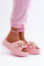 Pink platform summer flip-flops with decorative accents and foam sole, worn by person in matching pink pants for a casual look.