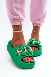 Green platform summer flip-flops with decorative gold accents, worn with pink pants, ideal for beach or holiday outings.