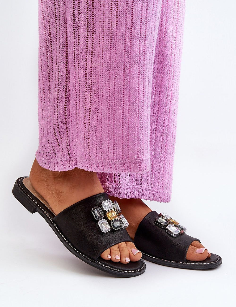 Person wearing Velinor Decor flat sandals with decorative accents, featuring a glossy synthetic upper and soft leather insole.