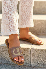 Woman wearing Naerelle Suede Spark Flip-Flops with sequins, pairing them with white lace pants on stone steps.
