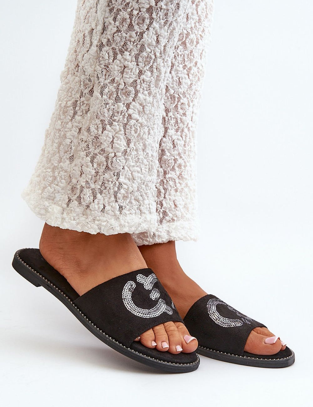 Black suede flip-flops with sequined design, worn with textured white pants.