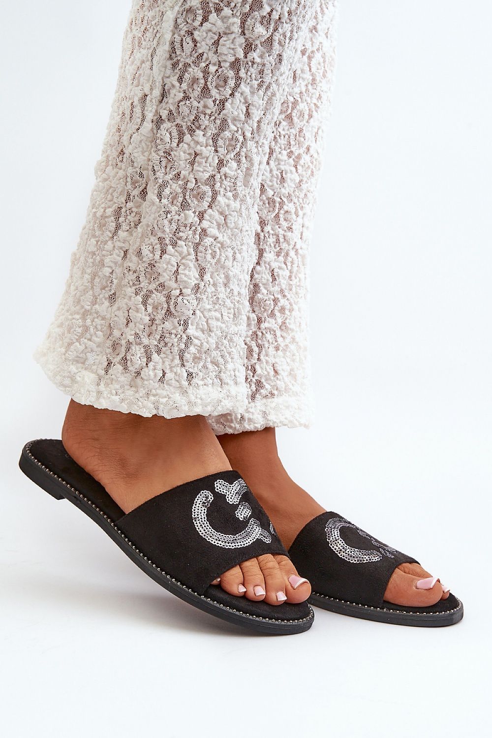 Black suede flip-flops with sequined design, worn with textured white pants.