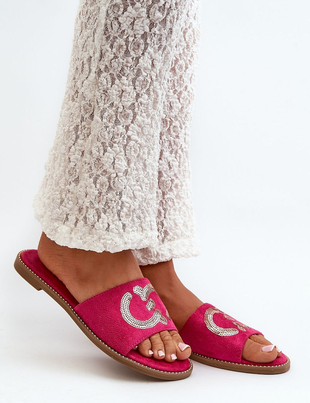 Woman wearing Naerelle Suede Spark Flip-Flops with sequins, paired with textured white pants, showcasing summer style.