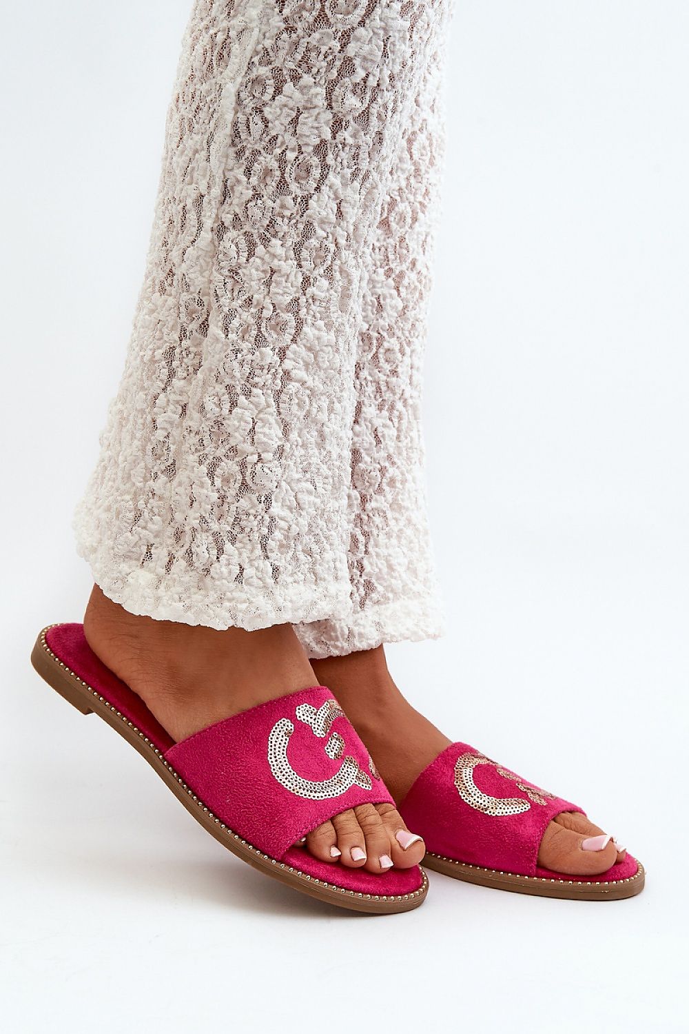 Woman wearing Naerelle Suede Spark Flip-Flops with sequins, paired with textured white pants, showcasing summer style.